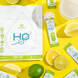 H2O Electrolytes™ Lemon Lime zero sugar electrolyte powder with fresh lemon and lime slices, powder mix, and a refreshing fizzy drink on a bright yellow background. Sugar-free hydration mix for daily wellness and endurance.