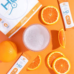 H2O Electrolytes™ Orange zero sugar electrolyte powder with fresh orange slices, powder mix, and a refreshing bubbly drink on a bright orange background. Hydration electrolyte packets for energy and recovery.